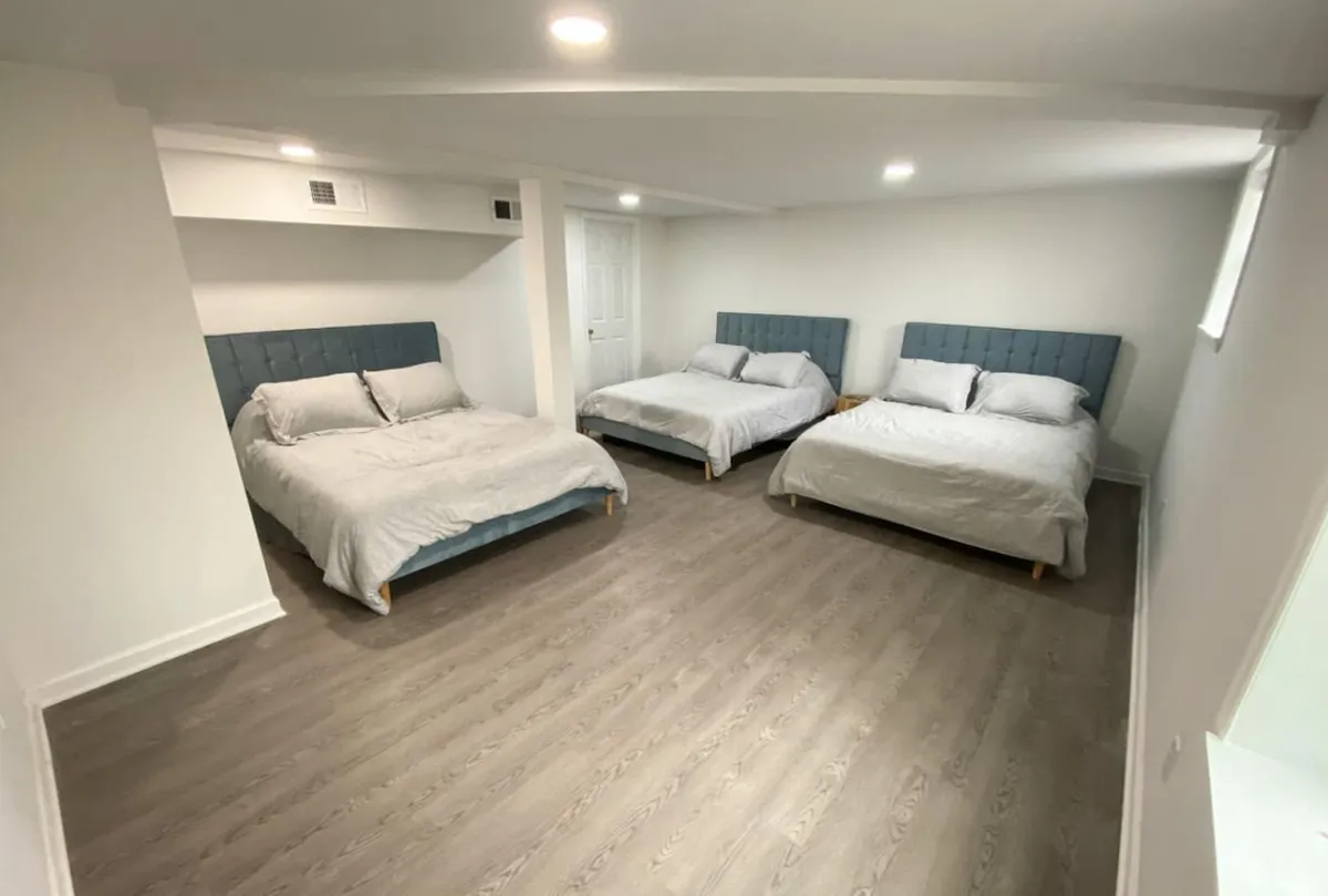 A spacious bedroom with three large beds featuring light-colored bedding and soft blue headboards. The room exudes comfort and offers plenty of natural light, making it ideal for families or groups. The layout allows for both relaxation and shared moments.