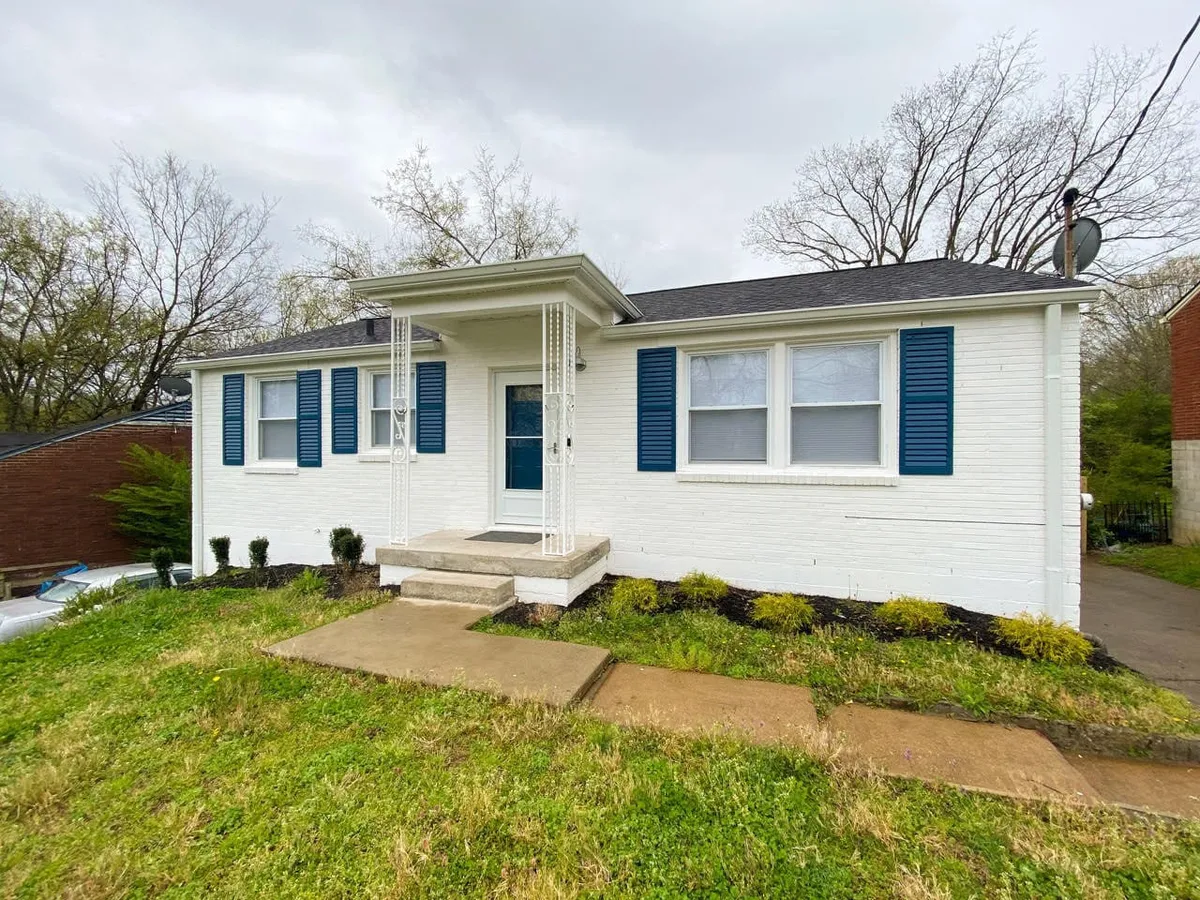 A charming exterior view of the home's front porch featuring blue shutters and a white brick facade. The inviting porch is set up for relaxing, with space for sitting and enjoying the outdoors, suggesting a welcoming return after a day of exploring.