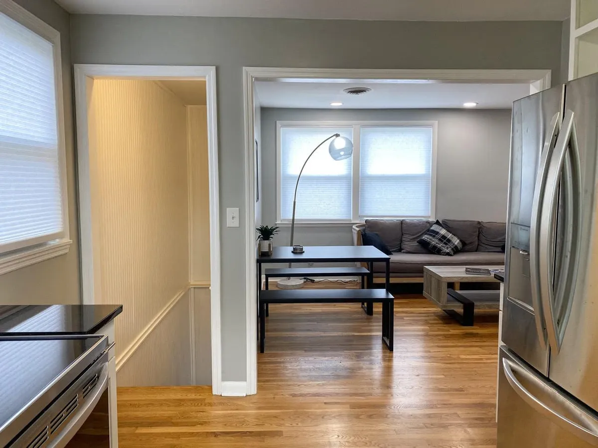 This image offers a wide view of an open-plan living area featuring a comfortable sofa, a dining table, and a modern kitchen with contemporary appliances. The scene is warm and inviting, with all major spaces—living, dining, and kitchen—visible and interconnected, emphasizing togetherness and social flow.
