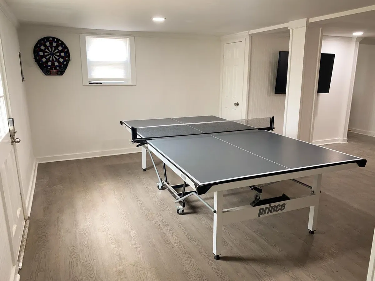 A lively, cheerful interior space featuring a ping pong table and dartboard, with natural light streaming in through the windows. The atmosphere is playful and family-friendly, inviting everyone to relax and enjoy games together.