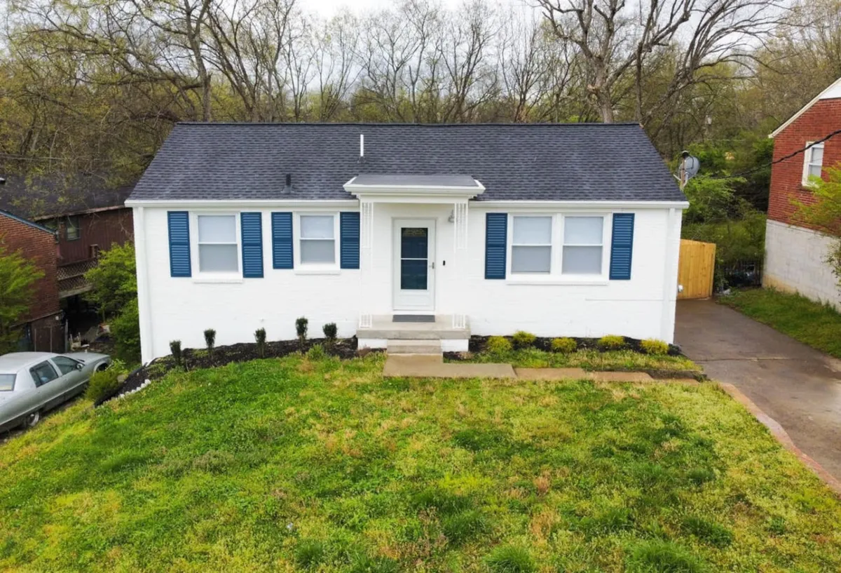 A bright and welcoming view of the home's white exterior with blue shutters, front steps, and a landscaped yard, suggesting a peaceful residential environment with easy access to gathering spaces.