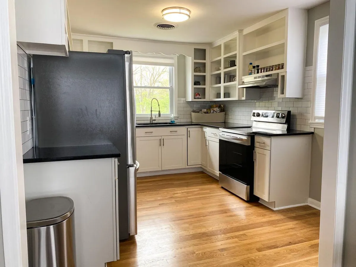 A bright, modern kitchen with stainless steel appliances, black countertops, white cabinetry, and a window flooding the space with natural light. The presence of a gas stove and functional workspace hints at gourmet possibilities and easy meal prep.
