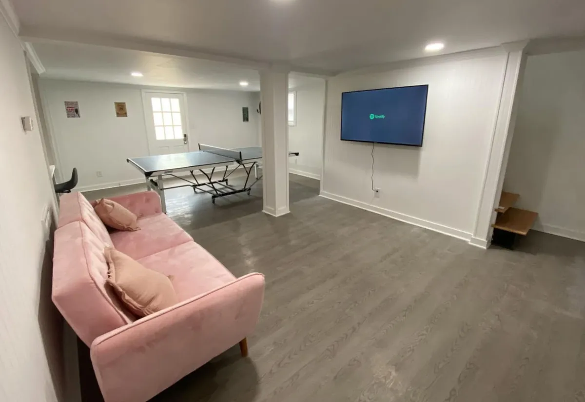 An inviting game room featuring a sleek pink couch, a ping pong table set up for play, and a wall-mounted TV. The space is decorated in a playful and relaxed style that encourages friendly competition and socializing.
