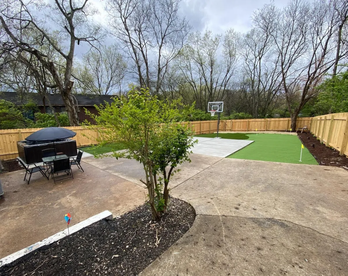 A backyard scene that includes patio furniture for outdoor lounging, a basketball court for playful activities, and a surrounding garden area. The space is set up for outdoor dining, relaxation, and enjoying the evening air, perfect for an intimate night under the stars.